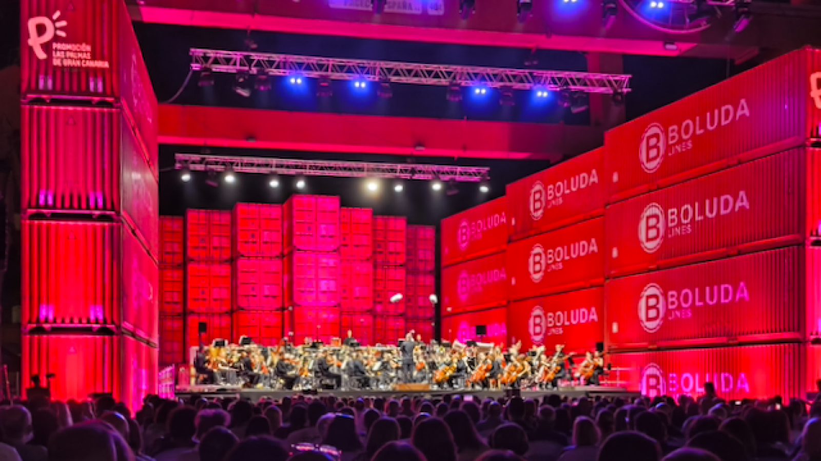 Sinfonieorchester auf der Bühne vor aufgestapelten Containern und Hafenkränen bei Nacht